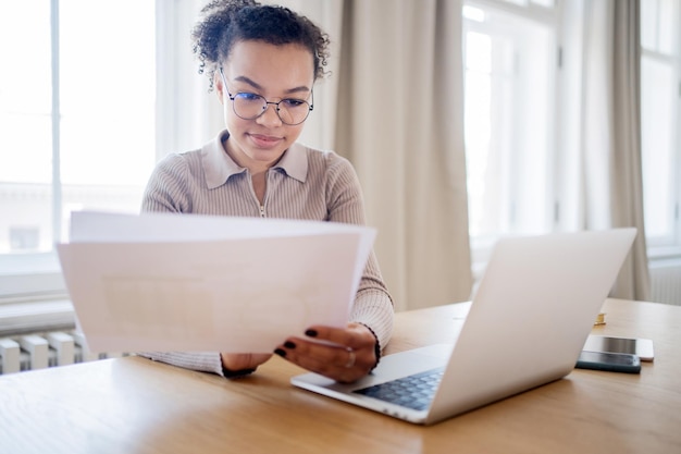 A student filling out the FAFSA form on a laptop, with various financial documents scattered on the table. The scene is well-lit, highlighting the importance of accuracy and attention to detail in the application process.