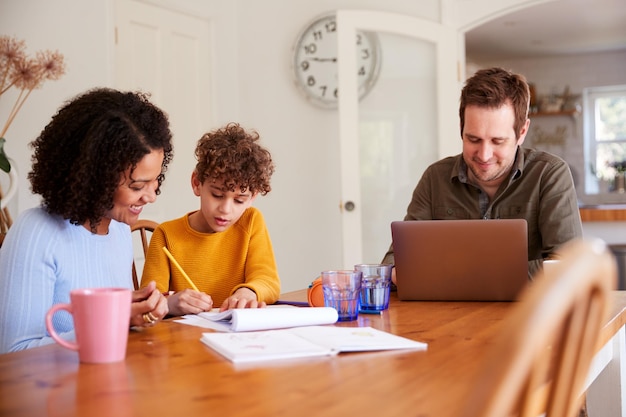 Two parents sitting at a table with their child, reviewing financial documents and a laptop displaying the FAFSA website. They are all smiling and engaged.